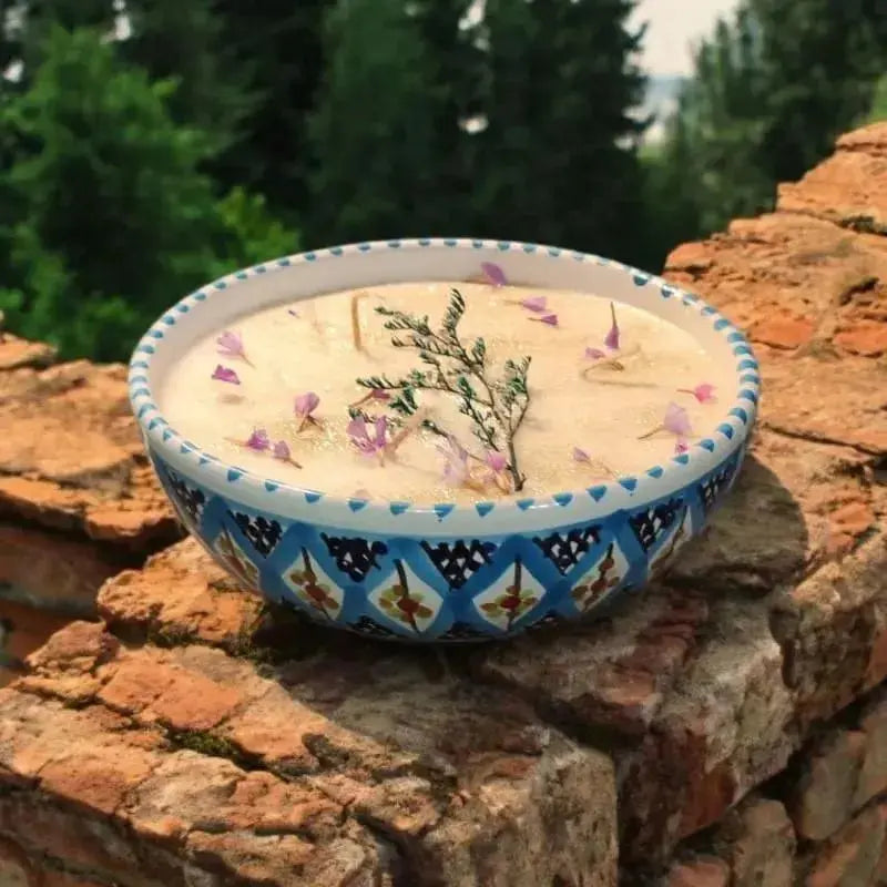 Bougie artisanale Lulu Baladine dans un bol bleu orné de motifs, décorée de fleurs séchées et de brindilles naturelles.