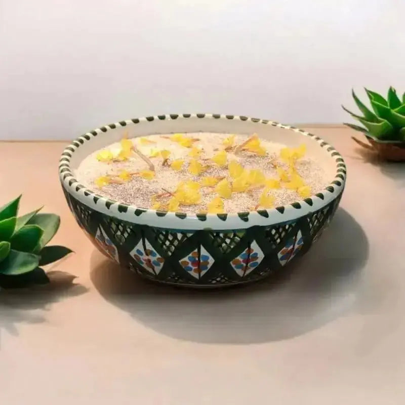 Bougie artisanale Lulu Baladine dans un bol vert décoré de motifs colorés, ornée de pétales jaunes séchés, posée sur une table claire avec plantes succulentes.