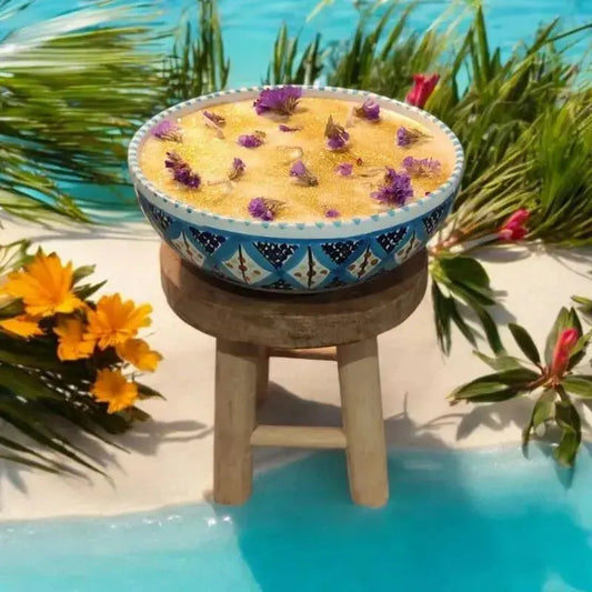 Bougie Ronde dans une ceramique tunisiene de nabeul pose sur un tabouret avec une bute de sable et de l'eau bleu clair