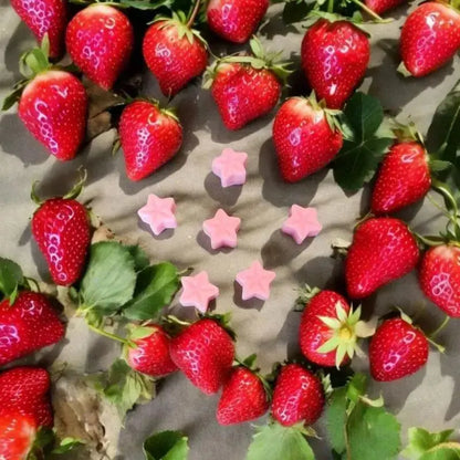 Fondant Parfumés fabriqué en Charente Maritime posé sur un tissu gris apportée de jolie fraises rouges bien mures