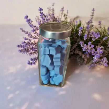 Fondant lavandes bleu dans un bocal posé sur une table blanche où derrière se situe de la lavande