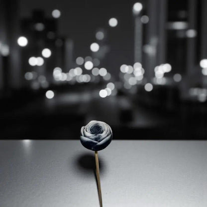 Petite renoncule bordée noir en cire artisanale, fleur décorative élégante sur fond urbain nocturne – Lulu Baladine