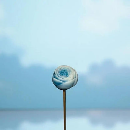 Petite renoncule bordée turquoise en cire artisanale, fleur décorative douce et apaisante sur fond bleu ciel – Lulu Baladine