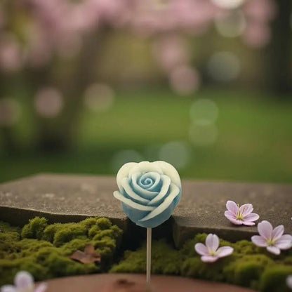 Rose bordée turquoise en cire artisanale, fleur décorative délicate posée sur un lit de mousse et de fleurs printanières – Lulu Baladine