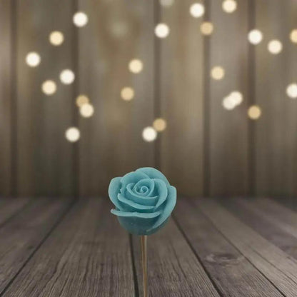 Rose turquoise en cire artisanale, fleur décorative posée sur fond en bois et lumières dorées – Lulu Baladine