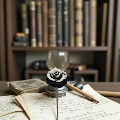 Rose moyenne bordée noire en cire artisanale, fleur décorative élégante posée sur un bureau ancien avec des livres – Lulu Baladine