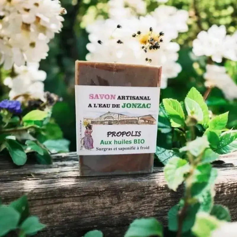 savon artisanal propolis saponifié à froid à l’eau de Jonzac posé sur bois au milieu de fleurs blanches