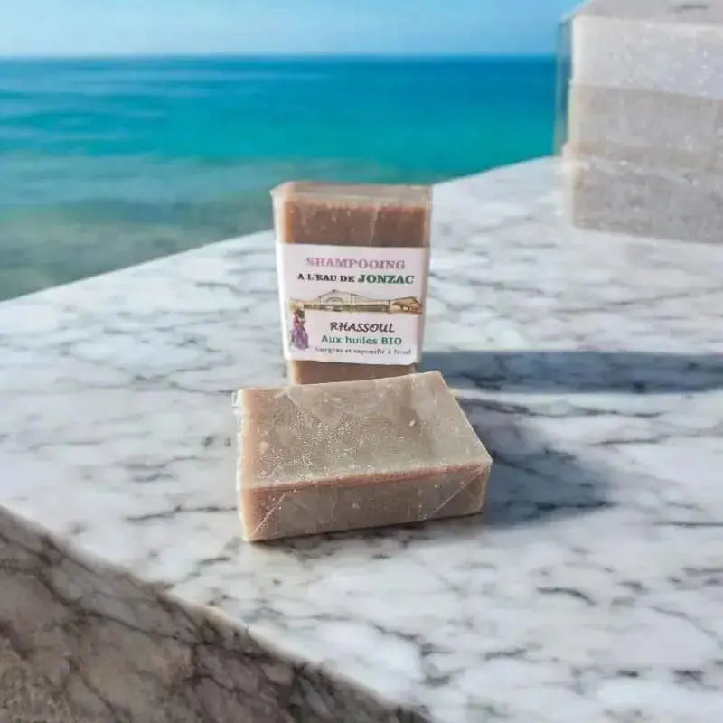 shampoing solide rhassoul saponifié à froid à l’eau de Jonzac posé sur plaque de marbre avec lumière naturelle et océan dernière 