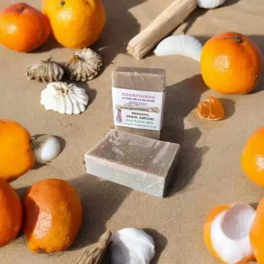 shampoing solide rhassoul agrumes saponifié à froid à l’eau de la ville  de Jonzac sur une plage avec des coquillage 